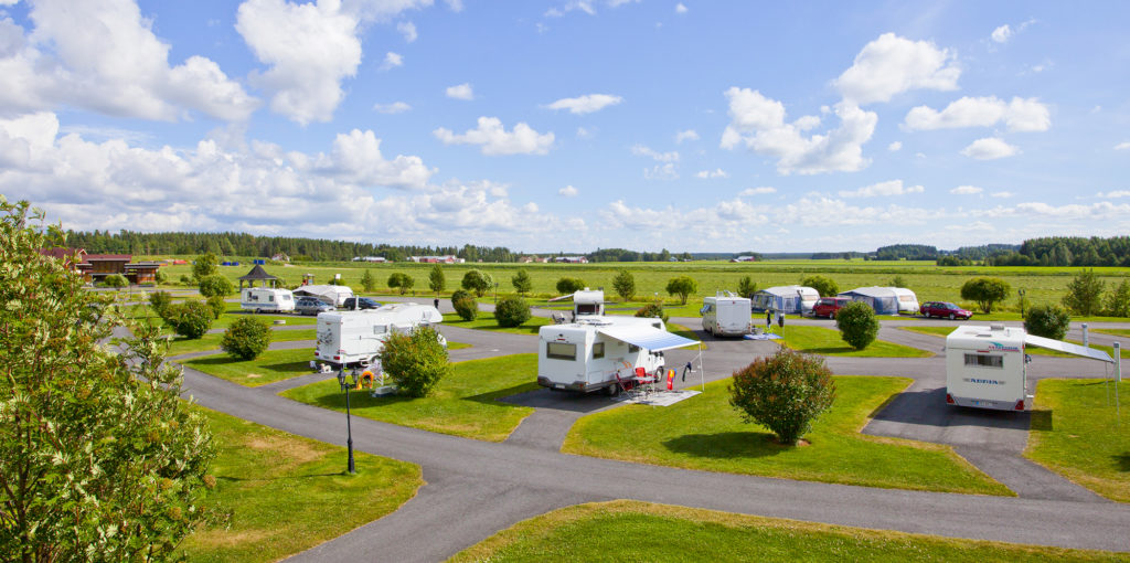 Vihreä aukea, leirintäalue, jossa matkailuautoja ja vaunuja kesäisellä säällä