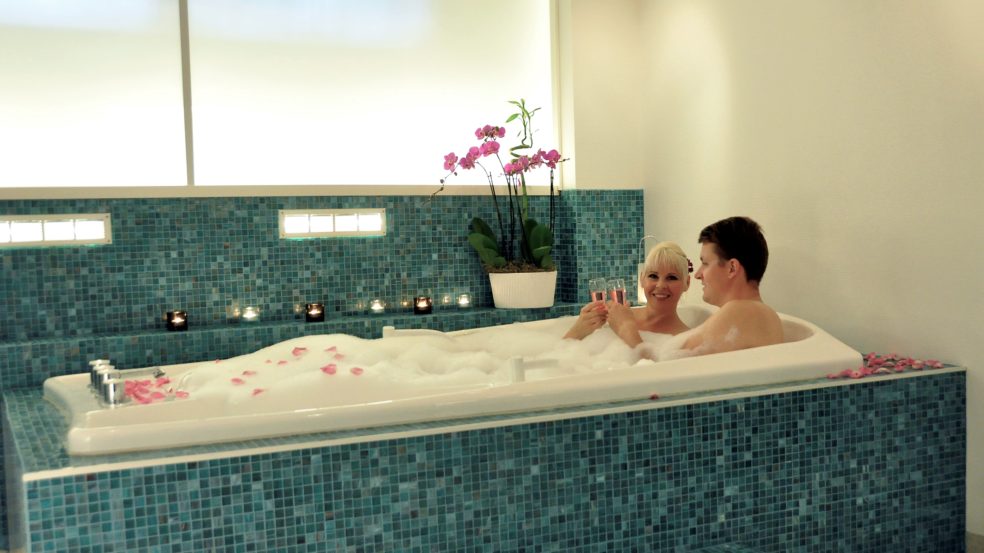 Pariskunta romanttisessa pariporeamme kylvyssä ruusunlehtien levätessä poreiden vaahdossa.