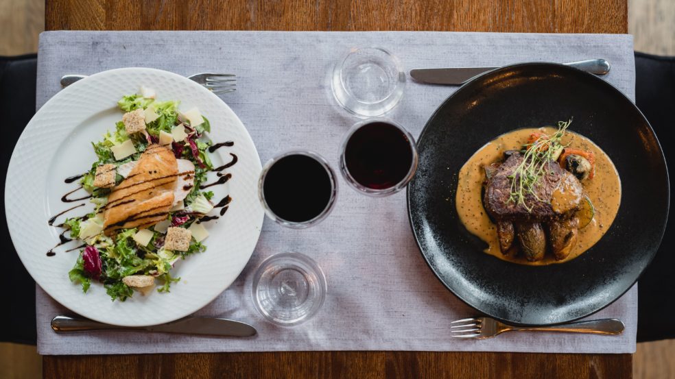 Ravintola Sorsanpesä a'la carte annokset pöydällä kuvattuna ylhäältä. Salaattia toisessa lautasessa ja lihaa kastikkeella toisessa.