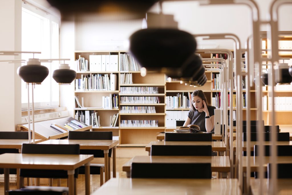 nainen lukee aalto kirjaston pöydällä Alvar Aallon suunnitteleman valaisimen alla