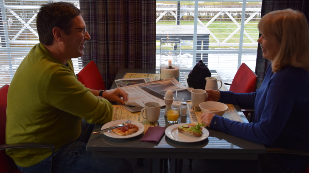 Kaksi henkilöä syö aamiaista hotellin oleskelutilojen pöydällä ikkunan ääressä.
