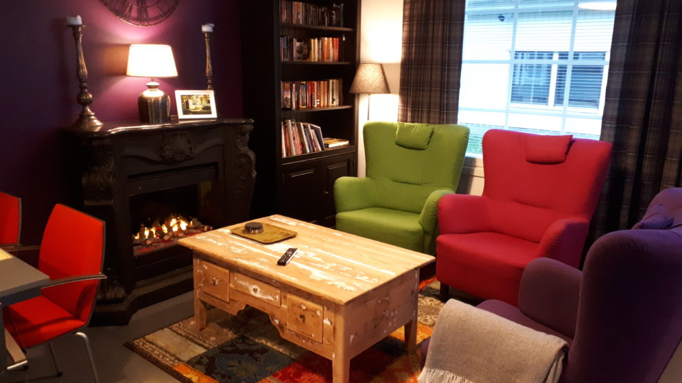 Hotelli HiljaHelenan kodikkaassa hotellihuoneesa mukavat nojatuolit, peitteet, takka ja kirjahylly luovat tunnelmaa.