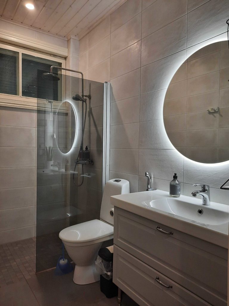 vessassa pyöreä peili, jonka takana valo. Heijastus suihkun seinämästä