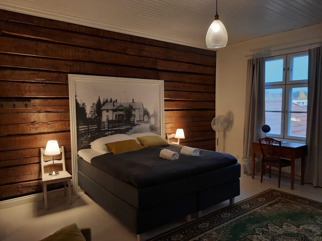 Kipinäkammari -parisänky, ruskea seinä ja sängynpäädyssä oleva suurennettu mustavalkoinen valokuva