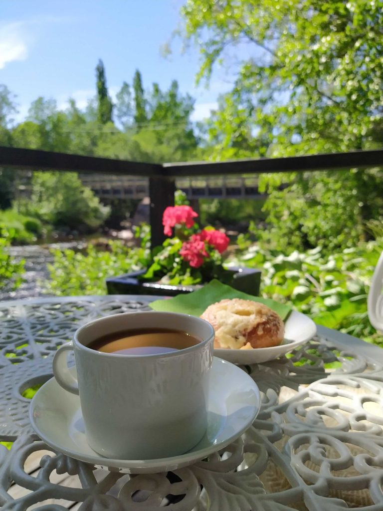 Annalan Villa Cafe & shop kuppi kahvia ja voisilmäpulla pöydällä terassilla, joka sijaitsee joen vieressä