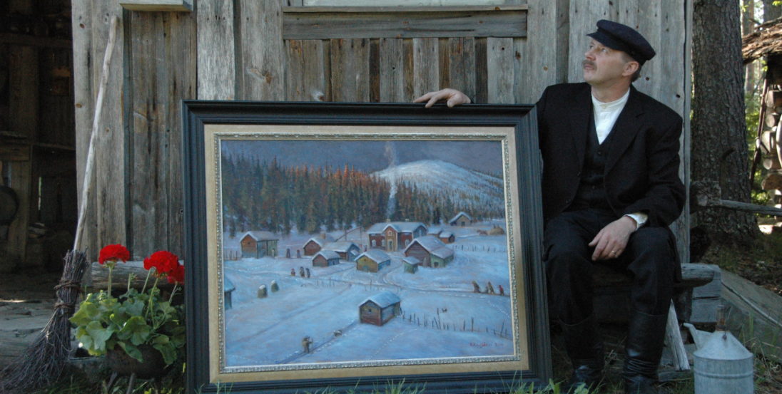 Taiteilija reijo Kivijärvi maalauksensa kanssa vanhan ladon edessä. Maalaus kuvaa perinteistä talvista kylämaisemaa