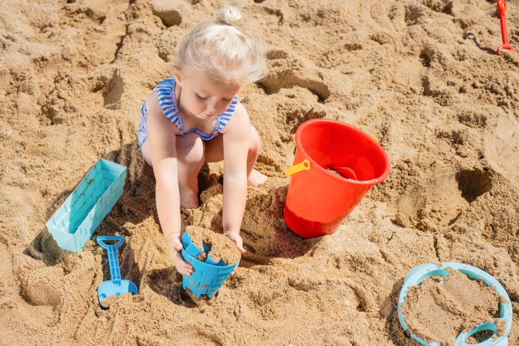 Lapsi leikkii hiekkaranalla ja tekee hiekkakakkua
